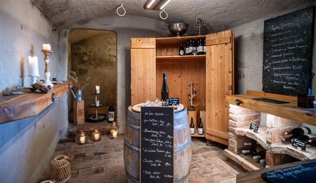 A cozy wine cellar with wooden shelves and a variety of wines. Candlelight creates an inviting atmosphere.
