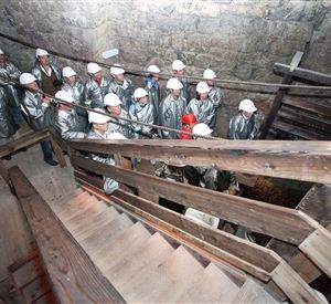 A group of people in silver suits and helmets stands on a staircase in a historic building. The walls are made of stone, and the atmosphere feels industrial and exciting.