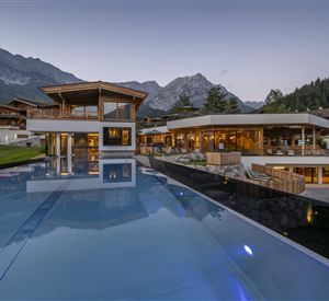 A modern building with large windows and a beautiful infinity pool. In the background, majestic mountains and trees are visible.