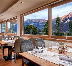 Een elegant restaurant met houten tafels en stijlvolle stoelen. De grote ramen bieden uitzicht op majestueuze bergen en een prachtig landschap.