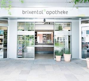 Een modern apotheekgebouw met grote glazen gevels en een uitnodigende ingang. Voor het gebouw staan planten in potten.