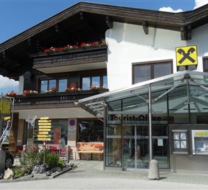 A modern building with a glass roof and an entrance to a bank. In the background, you can see a traditional chalet with flower boxes.