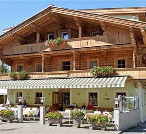 A rustic wooden building with a balcony and many flowers. There are outdoor seating options in front of the house.