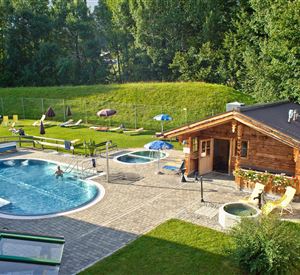 A beautiful outdoor area with a pool and hot tubs. In the background, there is a green meadow and a wooden hut.