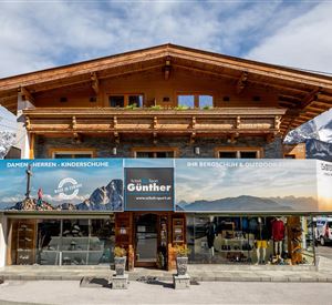 An old wooden building that houses a store for outdoor equipment. The shop displays large promotional banners and is located in a mountainous area.