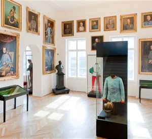 Een museum met historische portretten aan de muren. In het midden staat een vitrine met een uniform en een helm.