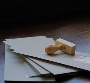 Een stapel neutrale papieren bladeren ligt op een tafel, naast een houten stempel. De stempel heeft een eenvoudige vorm en staat inline met de bladeren.
