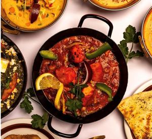Leckeres indisches Essen mit verschiedenen Currys und Beilagen. Das Hauptgericht in der Mitte enthält Hähnchen und frisches Gemüse.