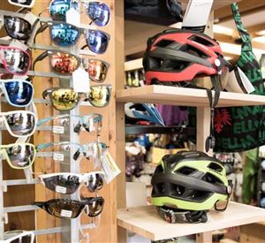 A selection of sunglasses and bicycle helmets is on display in a store. In the background, various accessories are visible.
