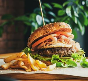 Ein großer Hamburger mit frischem Gemüse und Käse, serviert auf einem Holzbrett. Dazu liegen knusprige Pommes frites.