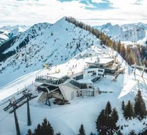 A picturesque mountain landscape with snow-covered peaks. In the foreground, a mountain station and chairlifts can be seen.