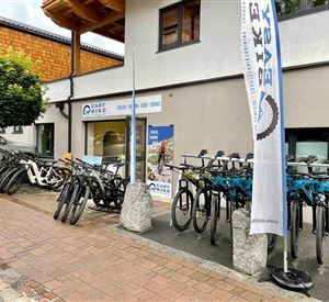 Ein Geschäft mit mehreren E-Bikes, die auf dem Gehweg ausgestellt sind. Über dem Geschäft weht ein Fahne mit dem Schriftzug "EASY BIKE".