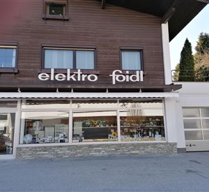Een moderne winkel met de naam "elektro foidl". De gevel is van hout en heeft grote ramen die een kijkje naar binnen mogelijk maken.