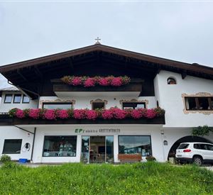 Een charmant huis met traditionele architectuur, versierd met kleurrijke bloemen. Op de voorgrond staat een auto geparkeerd, omringd door een groene weide.