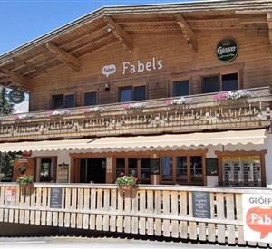 Ein schönes Holzgebäude mit einer einladenden Terrasse. Das Restaurant „Fabels“ hat ein rustikales Design und ist von Bäumen umgeben.