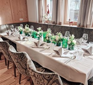 Een mooi gedekte tafel met groene bloemen en elegante glazen. De gezellige sfeer wordt benadrukt door de inrichting en de raamverlichting.