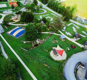 Ein weitläufiger Spielplatz mit verschiedenen Spielgeräten und Rasenflächen. Viele Bäume und ein ruhiger Weg umgeben den Bereich.