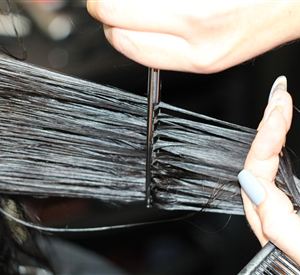 Eine Hand schneidet mit einer Schere Haare. Die Haarsträhnen sind glatt und glänzend.