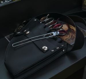 A black apron with various hairdressing accessories is placed on a table. Beneath it lies a brochure with hair stylings.
