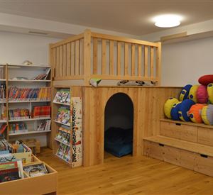 Een uitnodigende ruimte met een leeshoek, boekenkasten en een gezellige terugtrekplek. Kleurrijke kussens bieden plek om te zitten en te ontspannen.