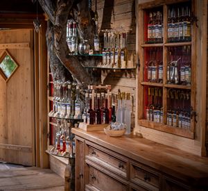 Een gezellige houten kamer met een houten commode en planken vol glazen. De deur op de achtergrond heeft een groen raam en nodigt uit naar buiten.