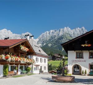 A picturesque alpine landscape with traditional wooden houses. In the background, majestic mountains rise under a clear blue sky.