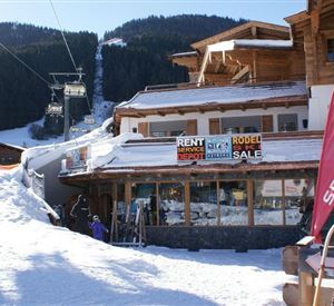 A snowy area with a mountain restaurant and ski rental. In the background, ski lifts and snow-covered mountains can be seen.