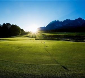 A beautiful golf course landscape at sunrise. The mountains in the background and the green grass create a serene atmosphere.