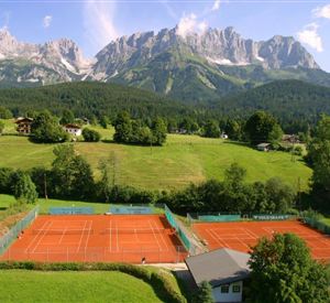 Een prachtige tennisfaciliteit met rode banen en een schilderachtig bergpanorama op de achtergrond. De omgeving is groen en uitnodigend, ideaal voor sportliefhebbers.