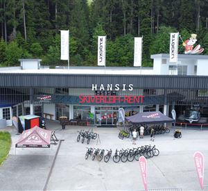 Een winkel voor sportartikelen met fietshuur en ski-uitrusting. Buiten staan verschillende fietsen en tenten.