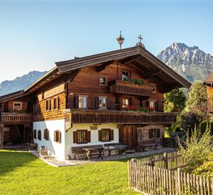 A traditional wooden house in the Alps with a well-kept garden. In the background, majestic mountains can be seen.