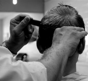 Ein Friseur schneidet die Haare eines Kunden. Man sieht die geschickte Hand der Person, die den Kamm benutzt.