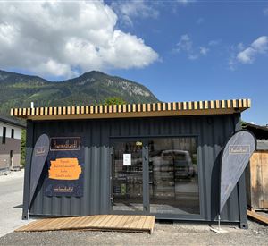 Een moderne winkel van containers in een landelijke omgeving. Op de achtergrond zijn bergen en een blauwe lucht te zien.