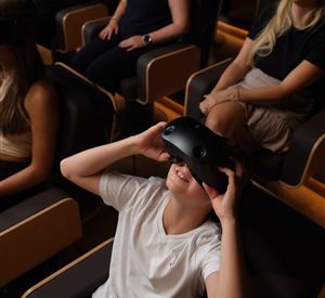 Een groep mensen zit in comfortabele stoelen en draagt virtual reality-headsets. Een kind glimlacht en geniet van de ervaring.