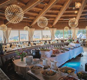Een elegant restaurant met houten balkenplafond en grote ramen. Een buffet met verschillende gerechten is gedekt, terwijl de decoratie eenvoudige, moderne meubels omvat.