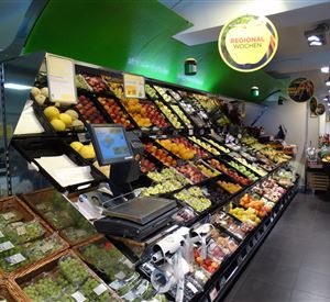 Ein farbenfrohes Obst- und Gemüseregal in einem Supermarkt. Frische, saisonale Produkte sind übersichtlich angeordnet.