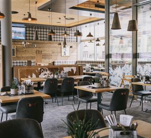 Ein modernes Restaurant mit Holzinterieur und gemütlicher Atmosphäre. Die Tische sind elegant gedeckt und es gibt viele Pflanzen.