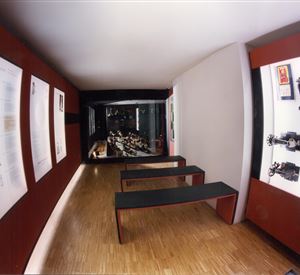 A modern exhibition space with exhibits on the walls and seating in the center. The lighting is dimmed, creating a cozy atmosphere.
