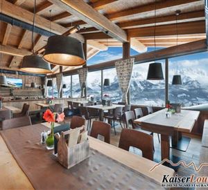 Ein gemütliches Restaurant mit Holzdekor und modernen Lampen. Große Fenster bieten einen Blick auf die Berge und lassen viel Tageslicht herein.