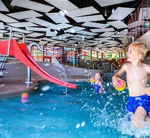 Een kinderbad met een rode glijbaan. Twee kinderen spelen in het water en spetteren vrolijk rond.