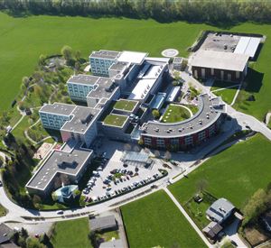 A modern building complex in a green landscape. The structure includes several separate buildings and is surrounded by lawns.