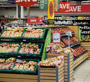 Een goed gesorteerde fruitstand in een supermarkt met veel kleurrijke appels. Op de achtergrond zijn andere producten en aanbiedingen te zien.