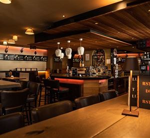 Een gezellige bar met houten interieur en dimbare verlichting. Het bargebied is goed gevuld en uitnodigend.