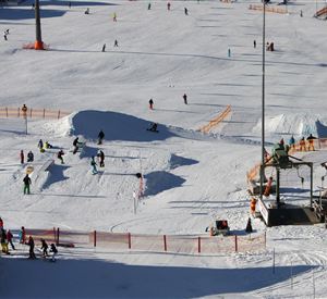 Eine lebhafte Wintersportlandschaft mit vielen Leuten, die Ski fahren und snowboarden. Der Schnee ist frisch und die Atmosphäre ist fröhlich.