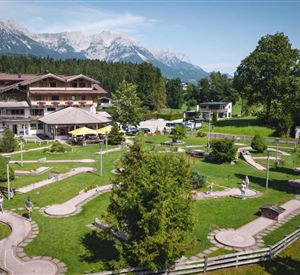 Eine schöne Mini-Golfanlage mit gepflegten Bahnen und viel Grün. Im Hintergrund sind Berge und ein Hotel zu sehen.
