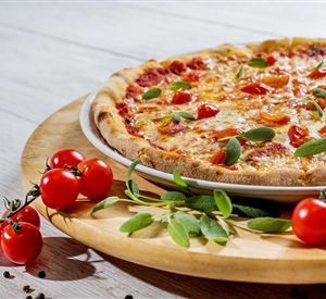 Eine köstliche Pizza mit frischen Tomaten und Kräutern auf einem holzigen Teller. Neben der Pizza liegen einige rote Tomaten und grüne Blätter.