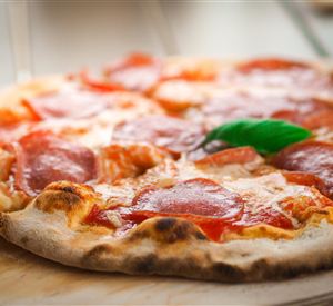 Een versgebakken pizza met salami en een groene basilicumblad-decoratie. De krokante korst en de gesmolten kaas maken het bijzonder smakelijk.