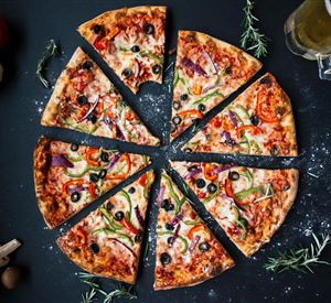 Eine köstliche Pizza, in Stücke geschnitten, mit Gemüse und Oliven. Im Hintergrund sind frische Zutaten und ein Glas Bier zu sehen.