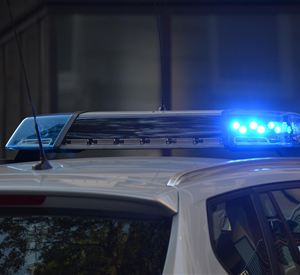 Ein Polizeiauto mit einem blauen Lichtsignal auf dem Dach. Es steht in einer urbanen Umgebung.