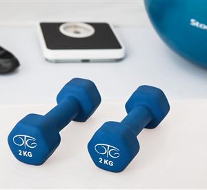 Two blue dumbbells weighing 2 kg are on a mat. In the background, there is a digital scale and a fitness ball.
